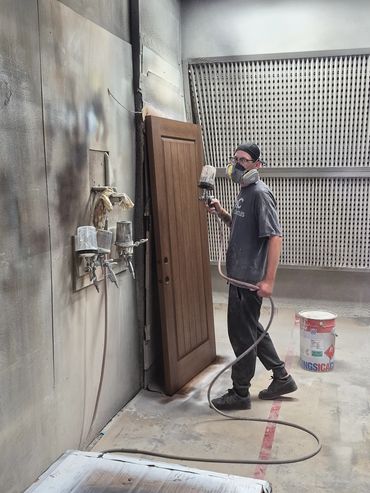 Man spray painting a wooden door in a workshop.