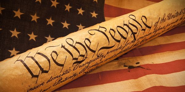 Close-up of the U.S. Constitution's 'We the People' text over an American flag.