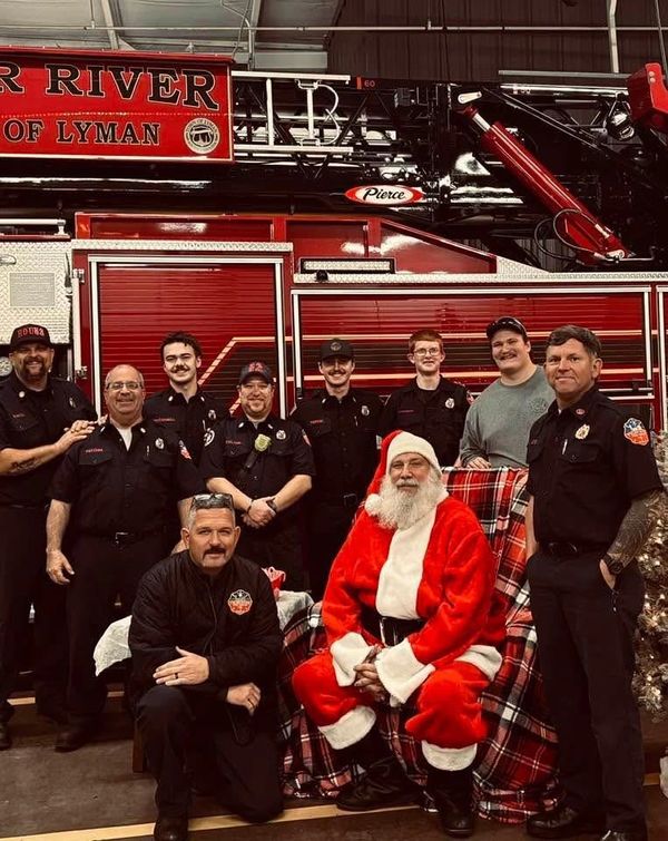 Firefighters pose with Santa Claus in front of a fire truck.