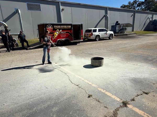 Person using fire extinguisher on a controlled fire in a parking lot.