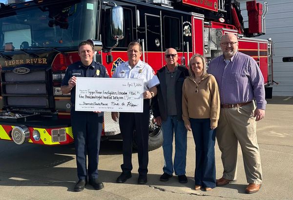 Group holding a donation check in front of a fire truck.