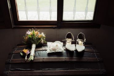 Wedding shoes, bouquet, and ring pillow arranged on a vintage chest.