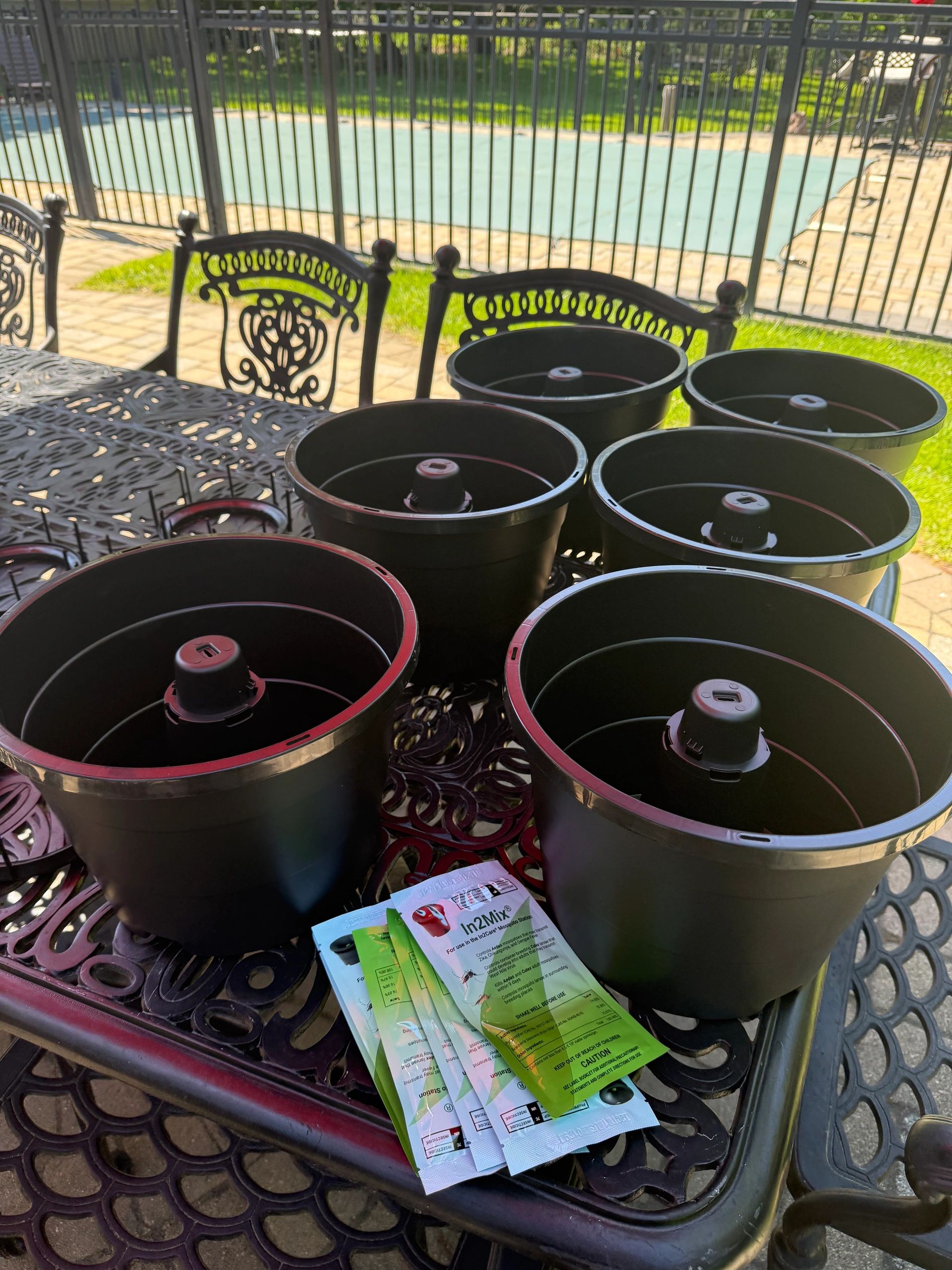 Black plastic pots and insecticide packets on an outdoor metal table.