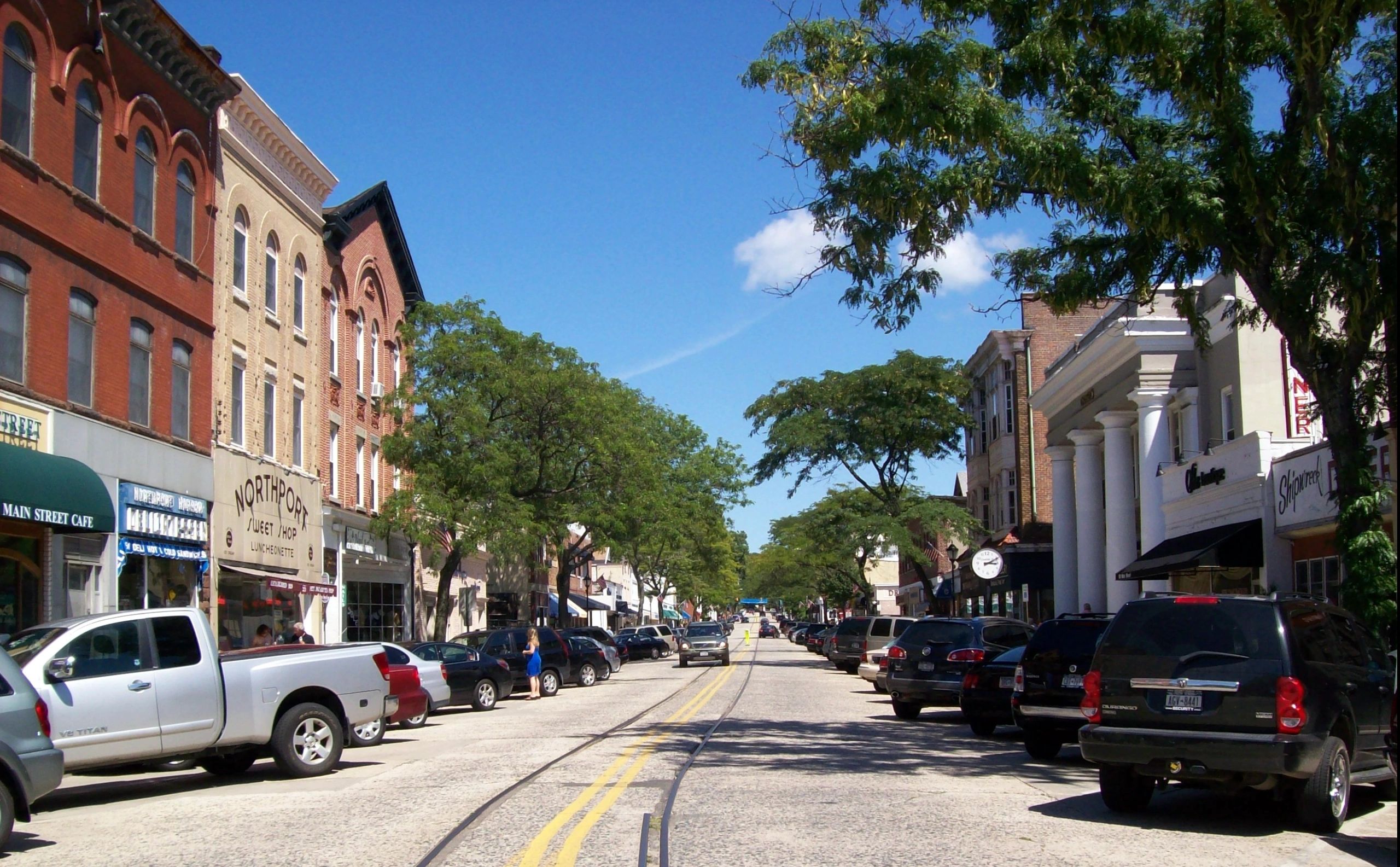 Sunny day on a bustling main street with parked cars and historic buildings.