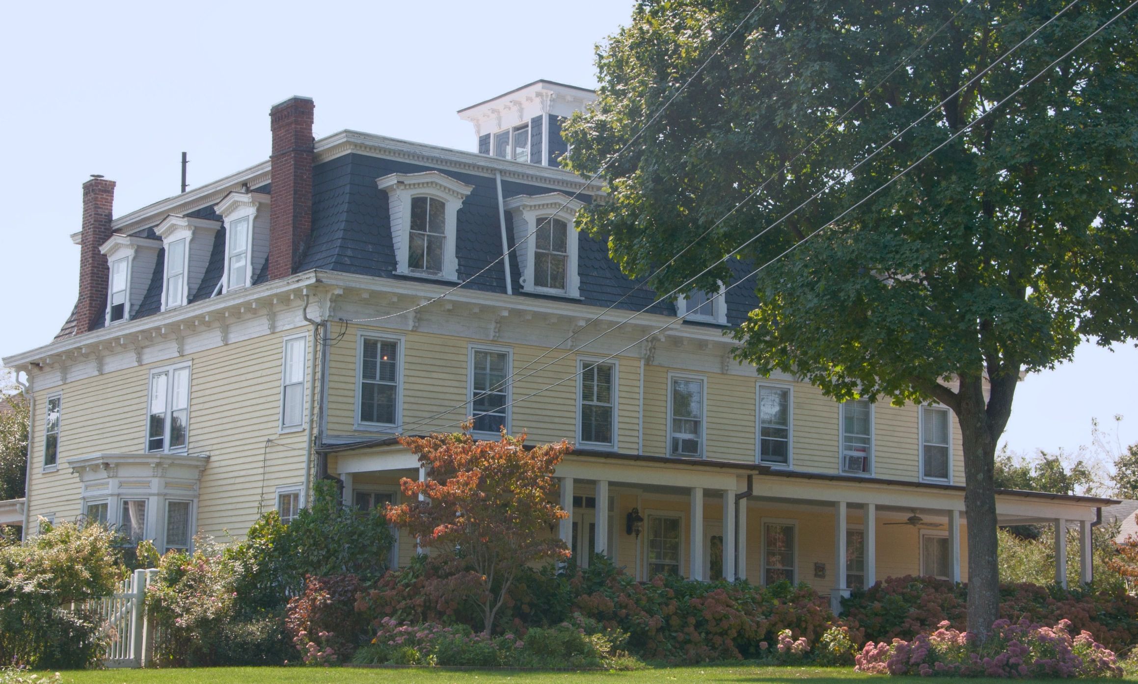 Large yellow Victorian house with a dark mansard roof and lush garden.