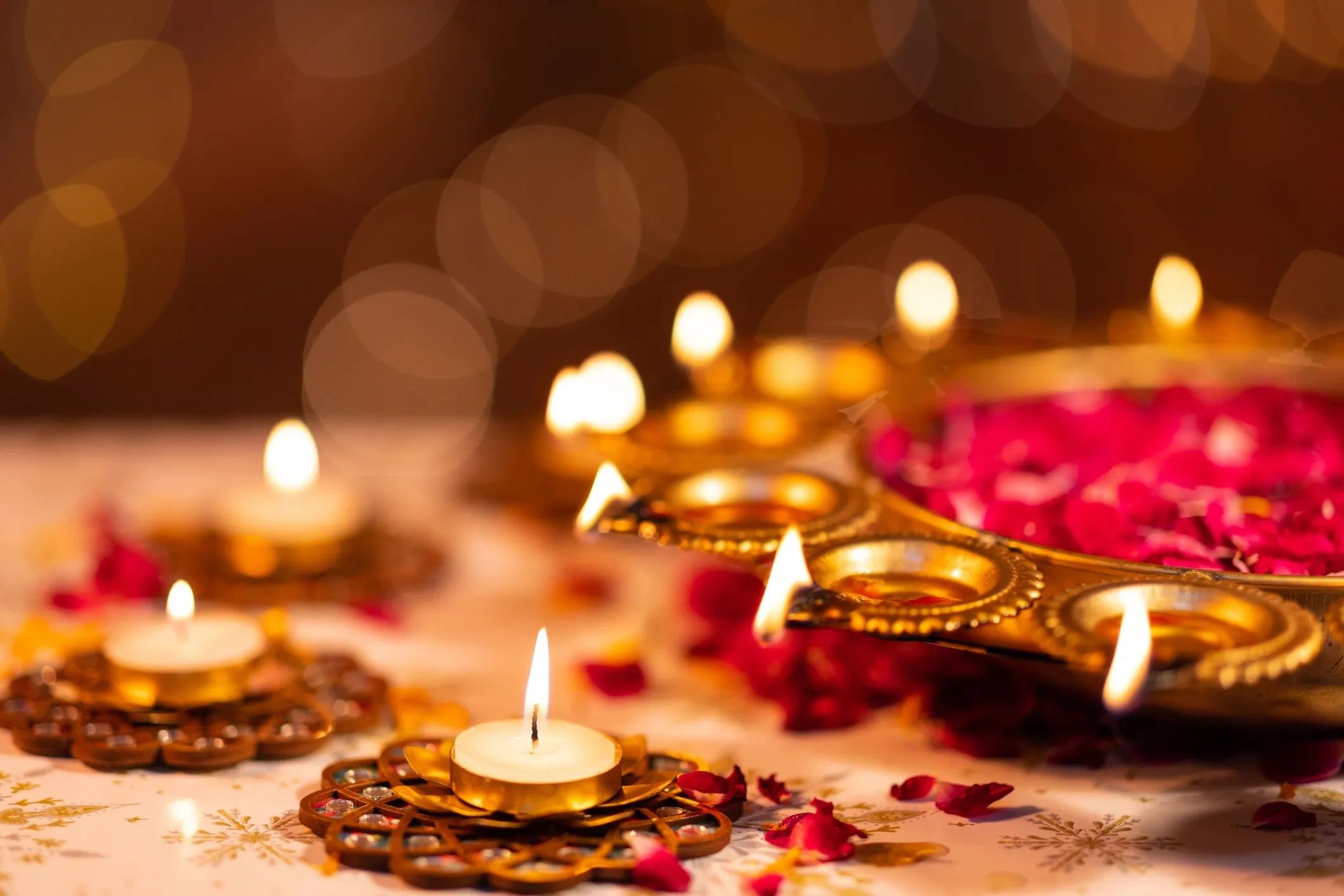 Lit candles in decorative holders with rose petals, creating a warm festive ambiance.