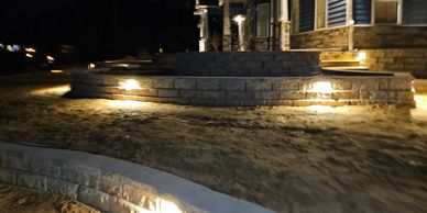 Outdoor stone retaining walls with embedded lights around a house at night.