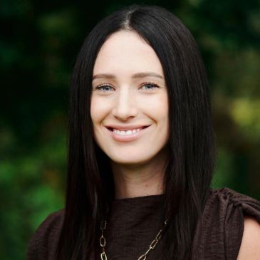 Woman with long dark hair smiling outdoors.