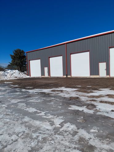 A warehouse with large white garage doors and icy ground under a clear blue sky.