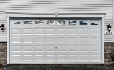 White paneled garage door with small decorative windows and exterior lights.
