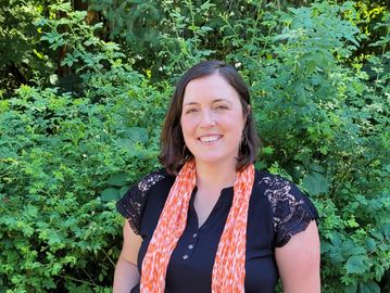 Woman smiling outdoors with greenery background.