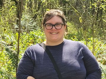 Smiling woman outdoors in a forested area.