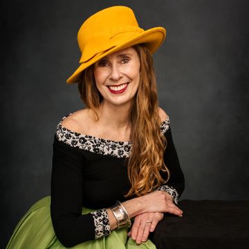 Smiling woman wearing a vibrant yellow hat and green skirt.
