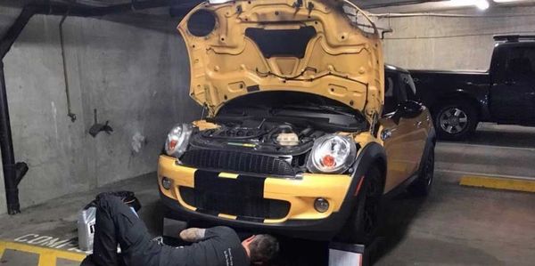 Man working under a yellow car in a parking garage.