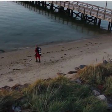 Person in red gear walking on a sandy beach near a wooden pier.