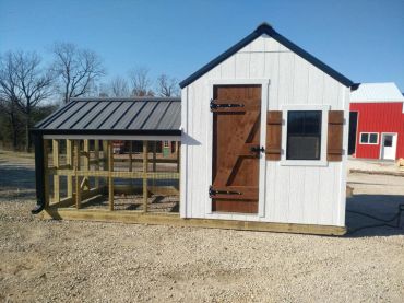 A small white chicken coop with a brown door and attached run on a gravel surface.