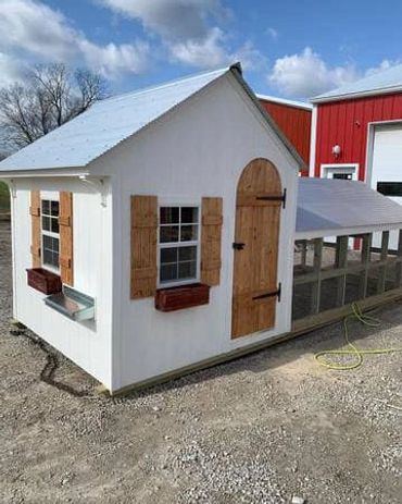 A small white coop with wooden shutters and a metal roof.