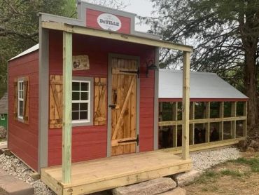 Red wooden chicken coop with a porch and enclosed run area.