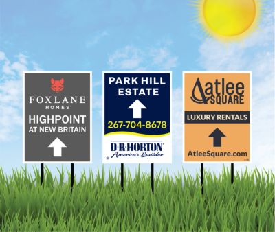 Three real estate signs on grass under a bright sun.