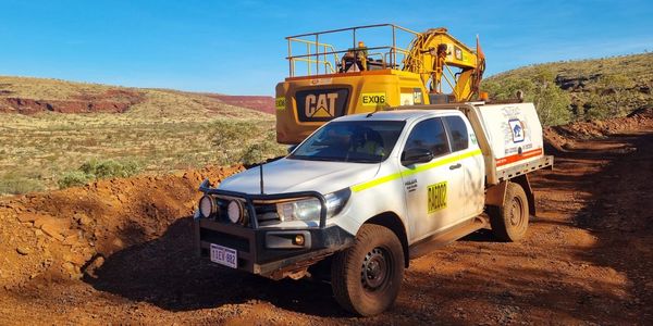 White utility truck parked near a yellow CAT excavator in a desert landscape.