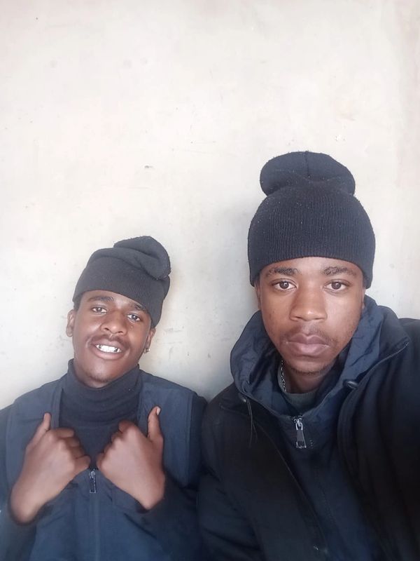 Two young men wearing black beanies and jackets posing for a photo.