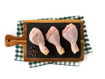 Three raw chicken drumsticks on a wooden cutting board with peppercorns.