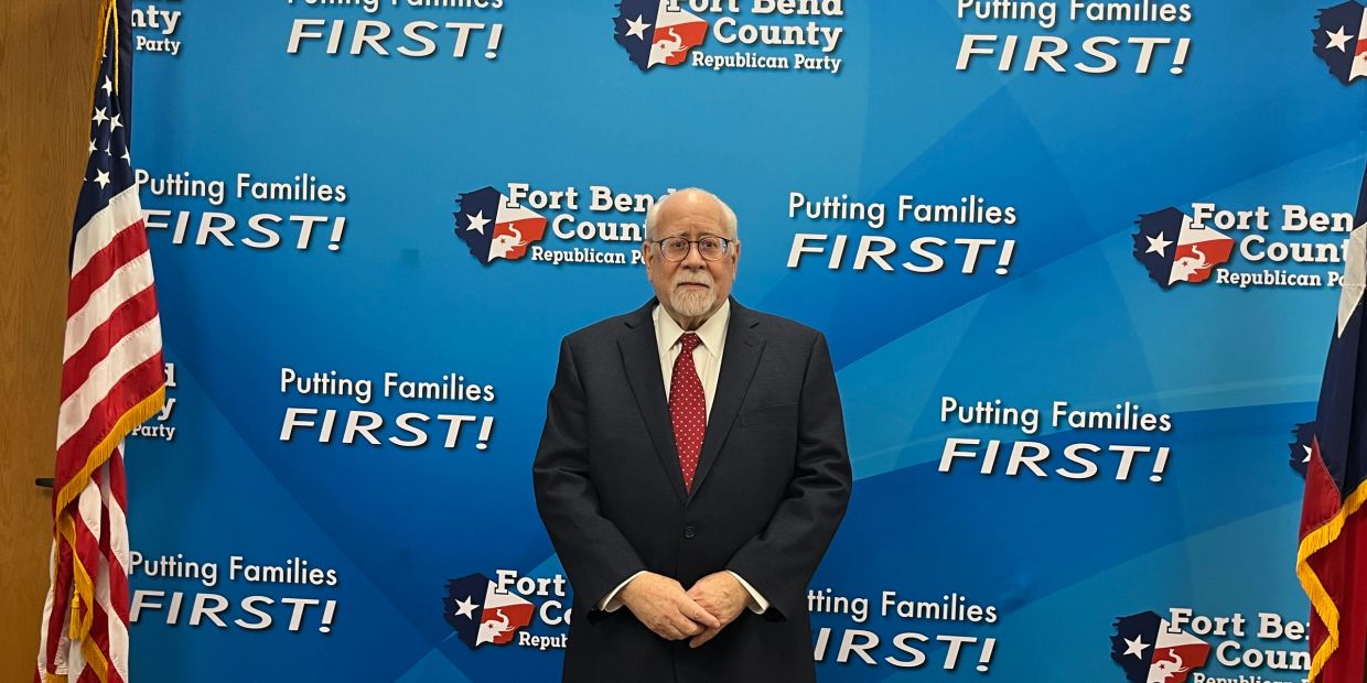 Man in suit standing in front of Republican Party banner.