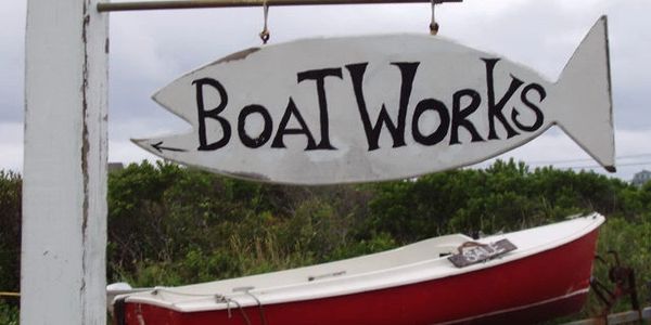 Wooden fish-shaped sign for Boat Works above a red and white boat.