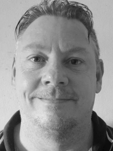 Black and white close-up portrait of a smiling man with short hair.