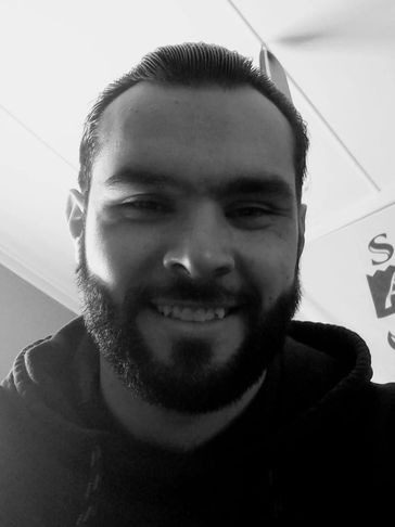 Black and white close-up of a smiling man with a beard and slicked-back hair.