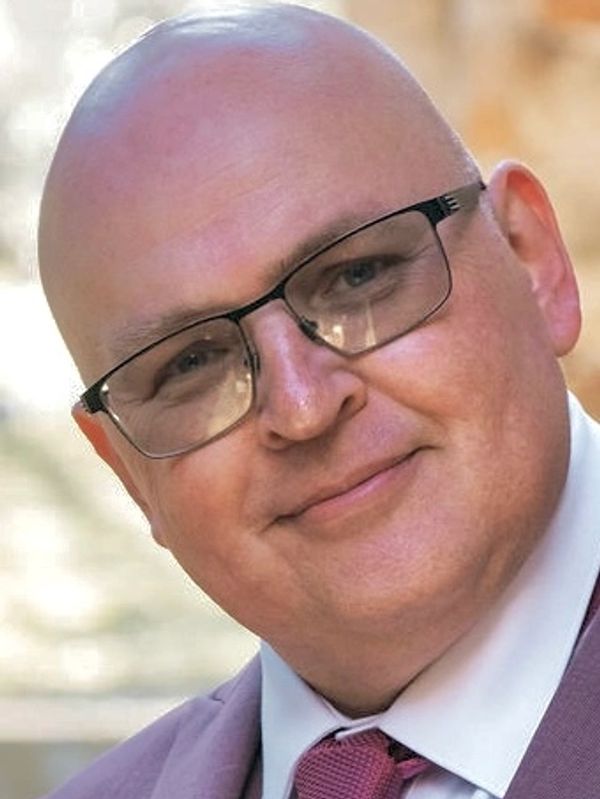Smiling bald man wearing glasses, a suit, and a tie.