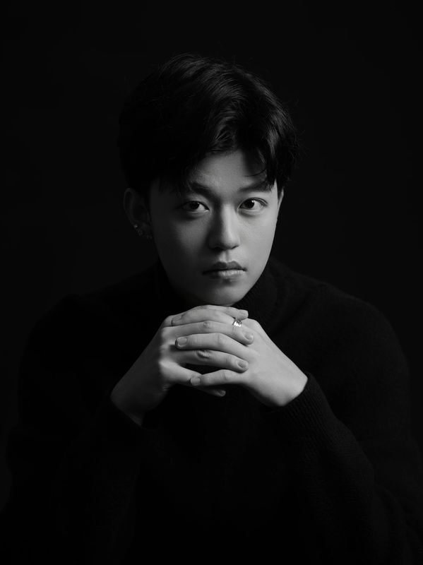 Black and white portrait of a contemplative young man with hands clasped.