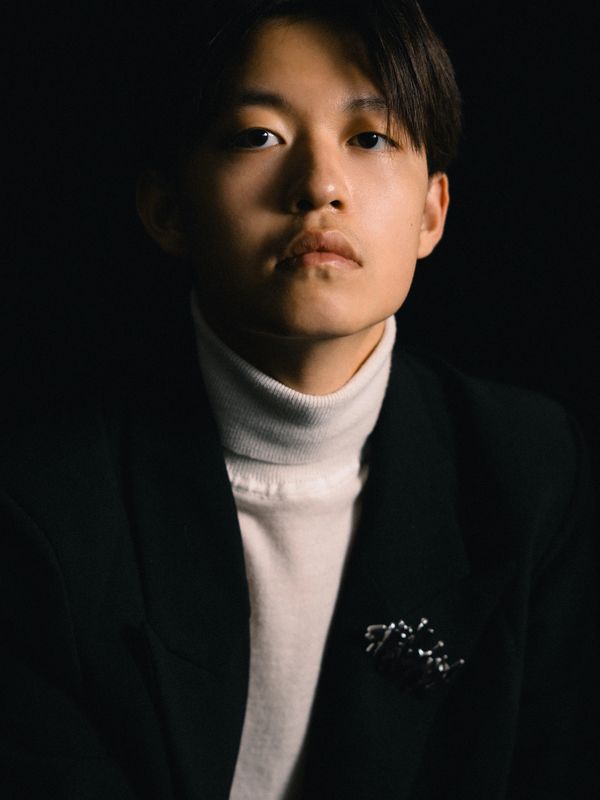 Portrait of a young person in a white turtleneck and black blazer with dark background.