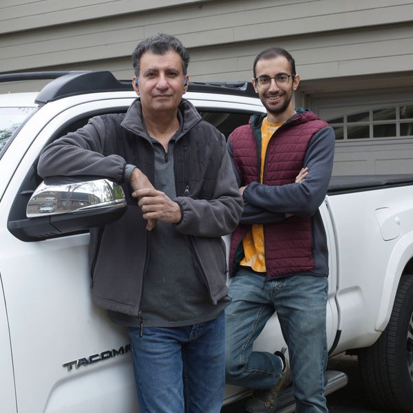 Two men posing casually by a white Tacoma truck in front of a house.