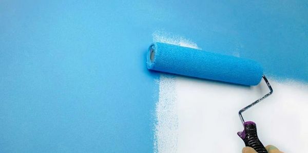 Painting a white wall blue with a paint roller.