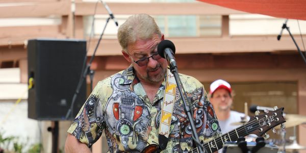 A man playing guitar and singing into a microphone outdoors.