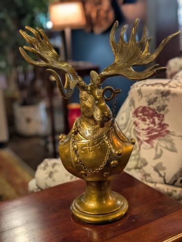 Decorative brass moose bust with detailed antlers and armor on a wooden table.