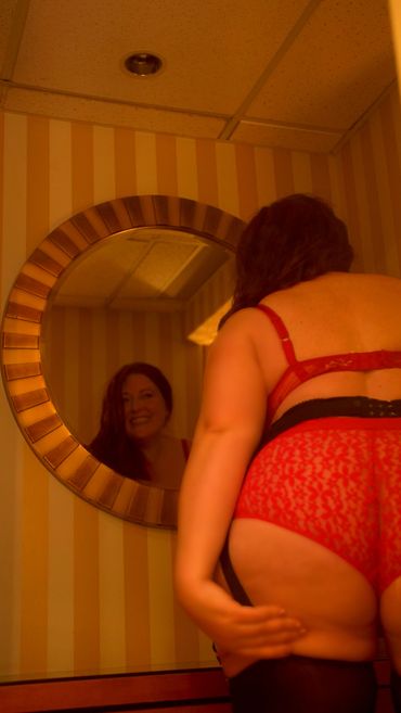 A woman wearing a garter belt and stockings smiles into a mirror 