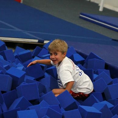 Young boy playing in a foam pit at a gym.