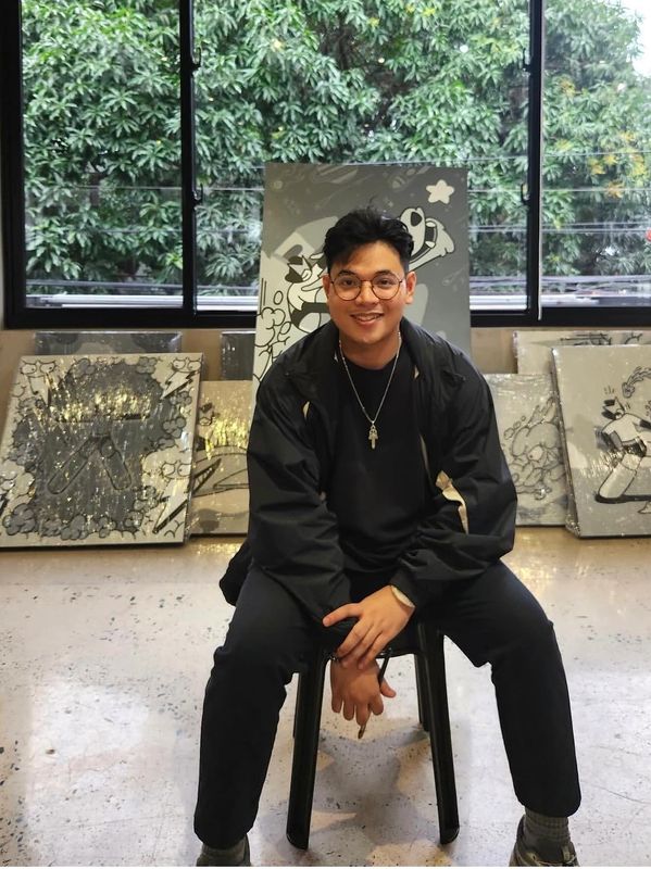 Smiling man sitting on a chair in front of artwork.
