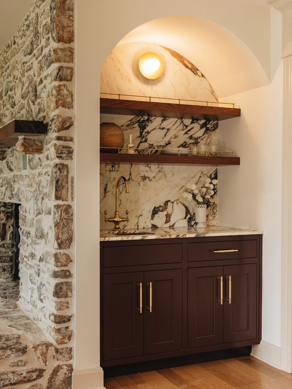 Cozy wet bar with marble backsplash, wooden shelves, and brass fixtures.