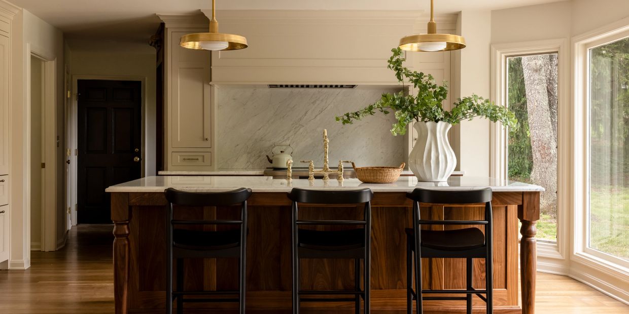 Elegant kitchen island with wooden stools, brass fixtures, and a large vase with greenery.