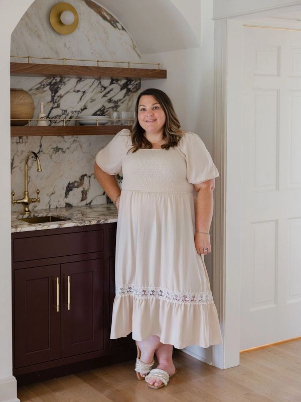 Woman in a cream dress standing in a kitchen.