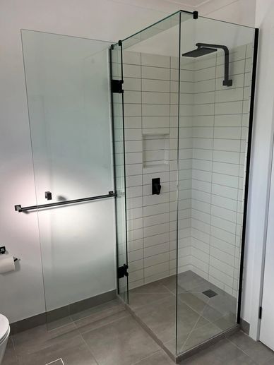 Modern glass shower enclosure with black fixtures in a minimalist bathroom.