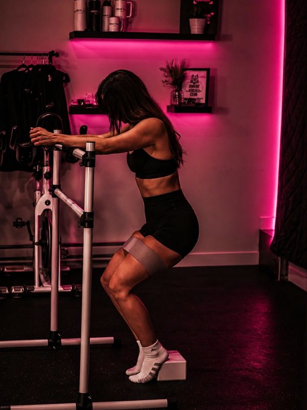 Woman exercising with resistance band and step box in a dimly lit gym.