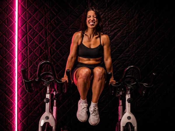 Woman in sportswear doing dips on stationary bikes with a focused expression.