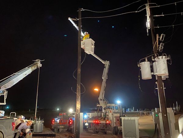 Workers repairing power lines at night using bucket trucks.
