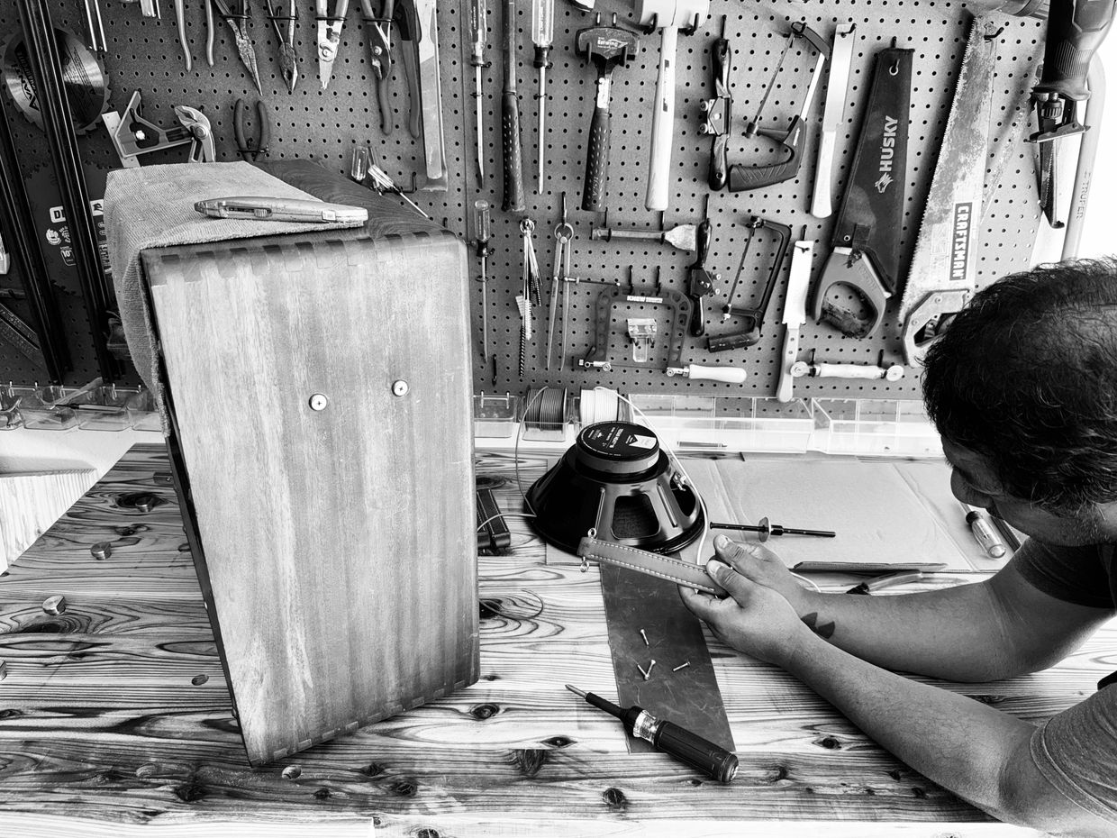 A man working on a wooden speaker cabinet in a well-equipped workshop.