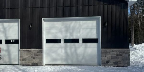 Modern white garage door with three horizontal windows on a black and stone exterior.