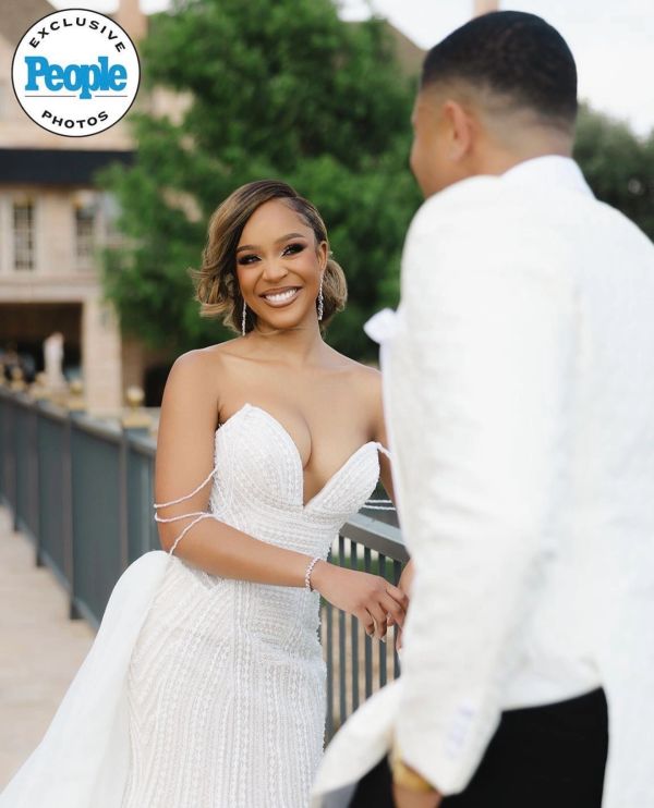 Bride in elegant white gown smiling at groom outdoors.